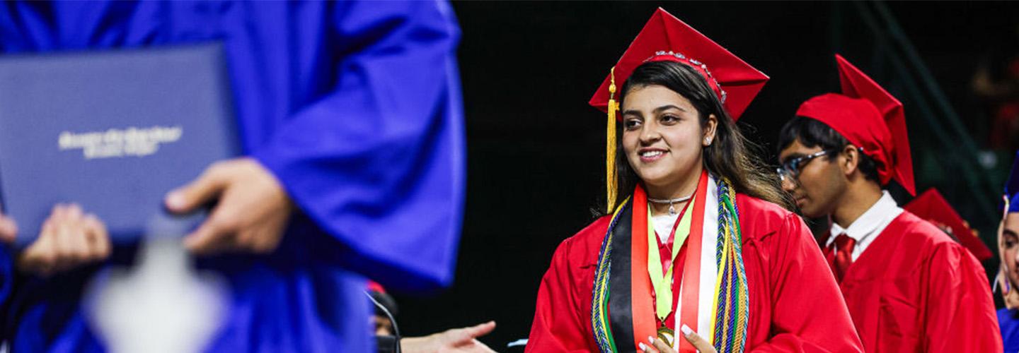 a young woman walks across the stage at graduation