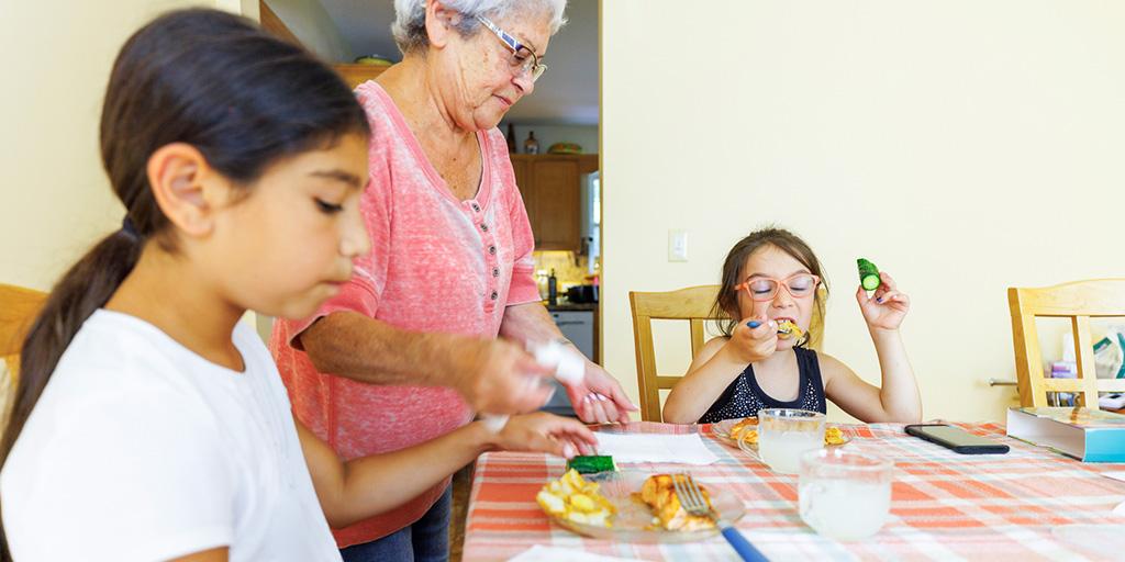 a grandmother feeds her grandchildren dinner