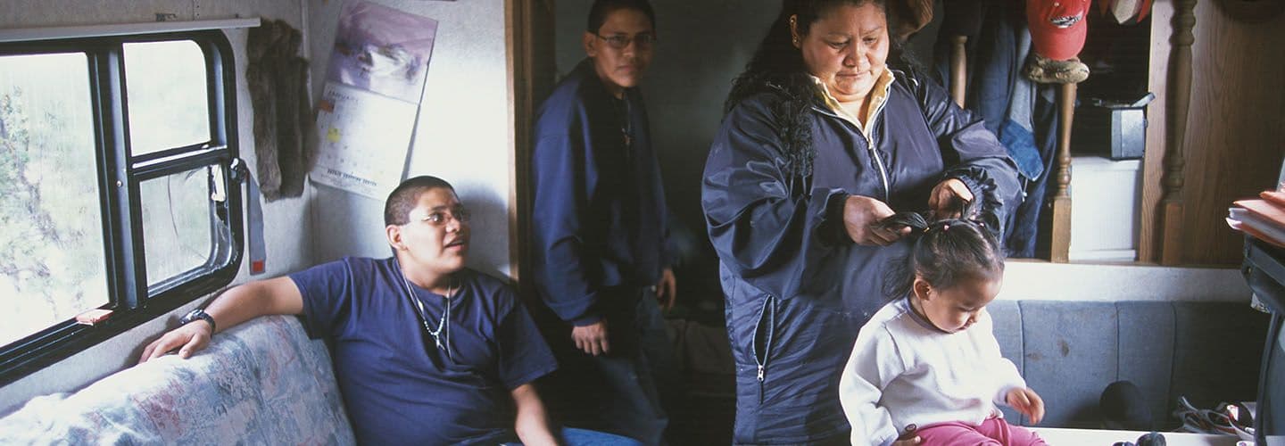 a woman braids a child's hair in their mobile home