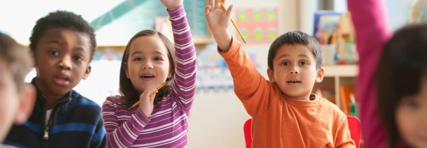 two young children raise their hands in class