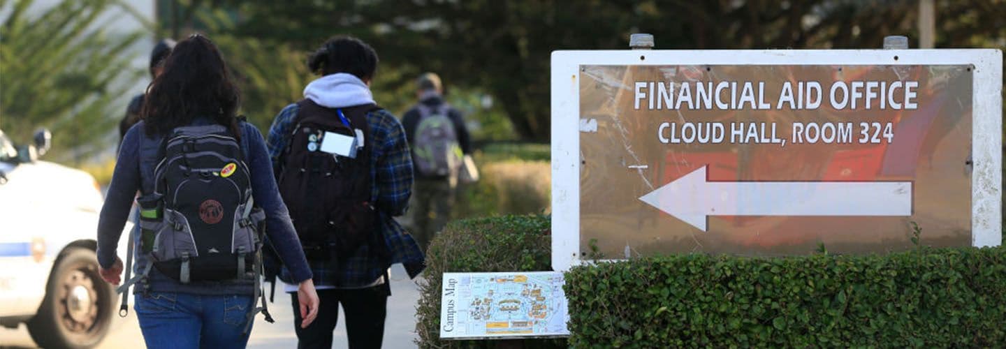 students walk past a sign for the school's financial aid office.